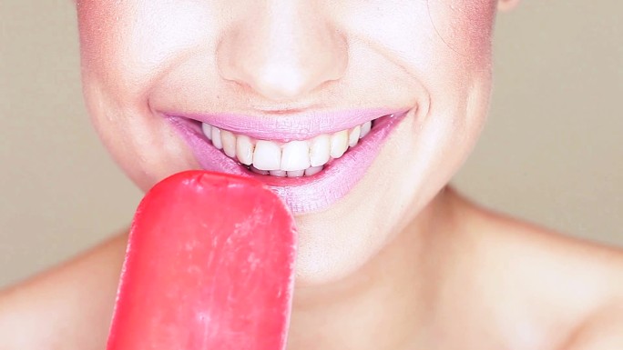 一个正在舔冰淇淋棒棒糖的迷人女人的嘴和舌头的感官特写