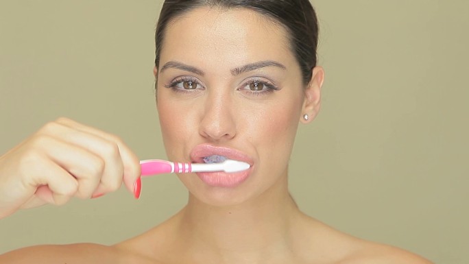 在浅棕色工作室背景下，一个微笑的美丽女人拿着牙刷和牙膏的特写镜头