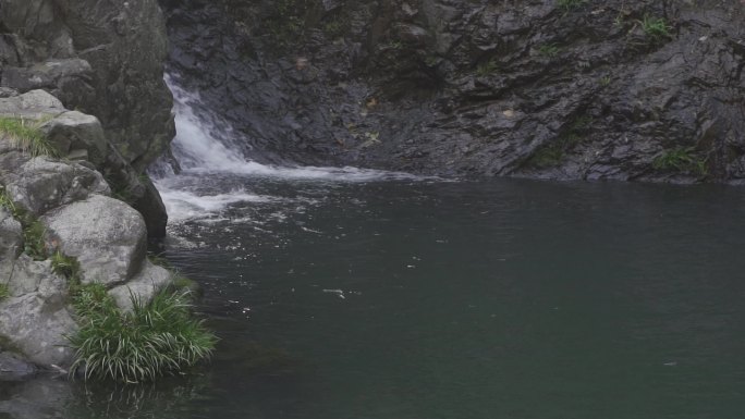 山石旁边瀑布流水进入绿色的深潭
