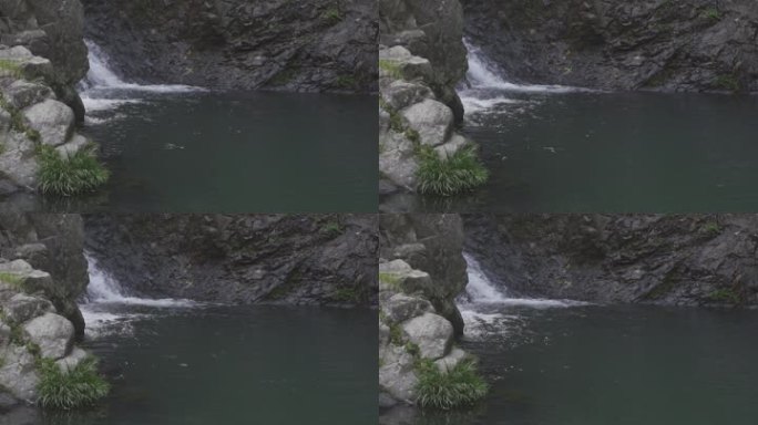 山石旁边瀑布流水进入绿色的深潭