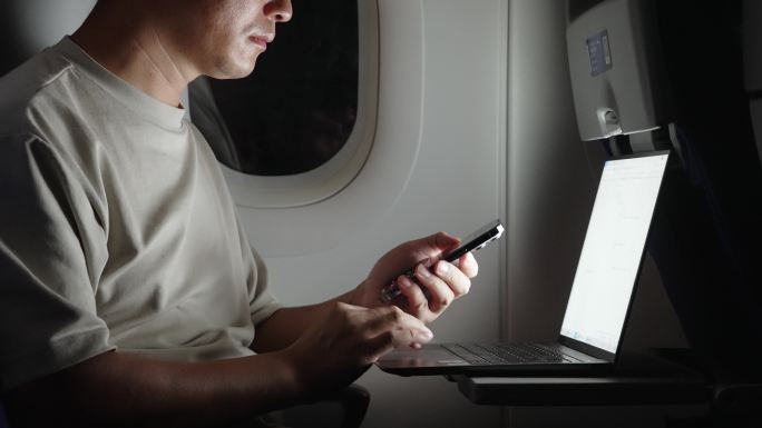 男子在飞机上使用手机和笔记本电脑