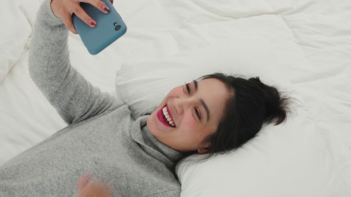 年轻美女躺在床上用手机打视频电话聊天
