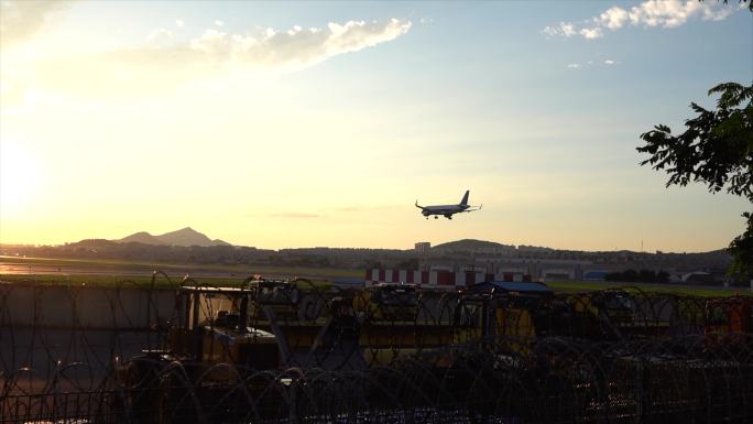日落时一架即将降落的飞机在机场跑道上空