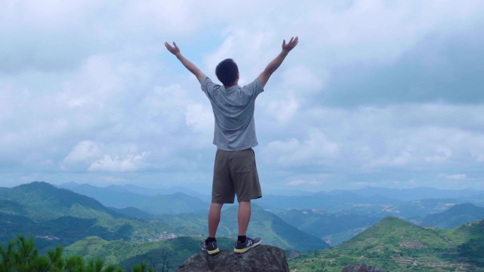 在山顶张开双臂感受自然的男人背影