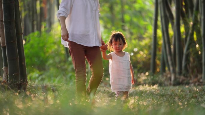 妈妈牵着女儿的手漫步在阳光公园欢乐亲子