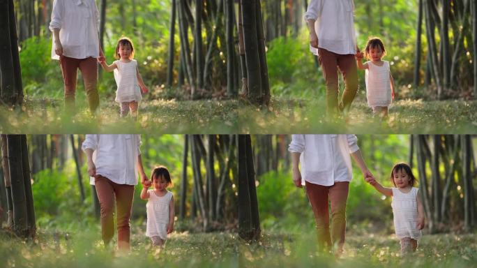 妈妈牵着女儿的手漫步在阳光公园欢乐亲子