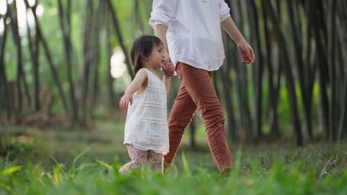 妈妈牵着女儿的手在公园里散步亲子欢乐时光