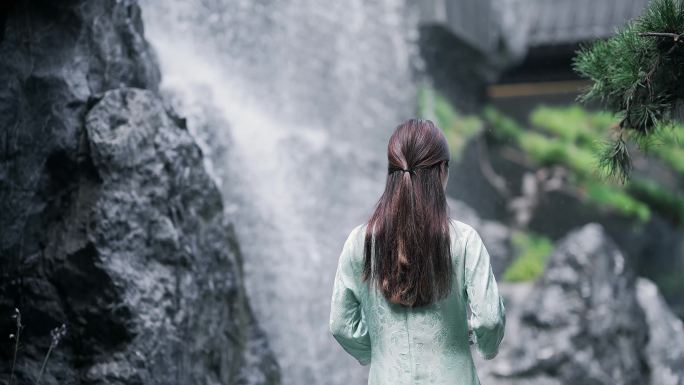 身穿汉服年轻女子走向园林景观水景墙上瀑布