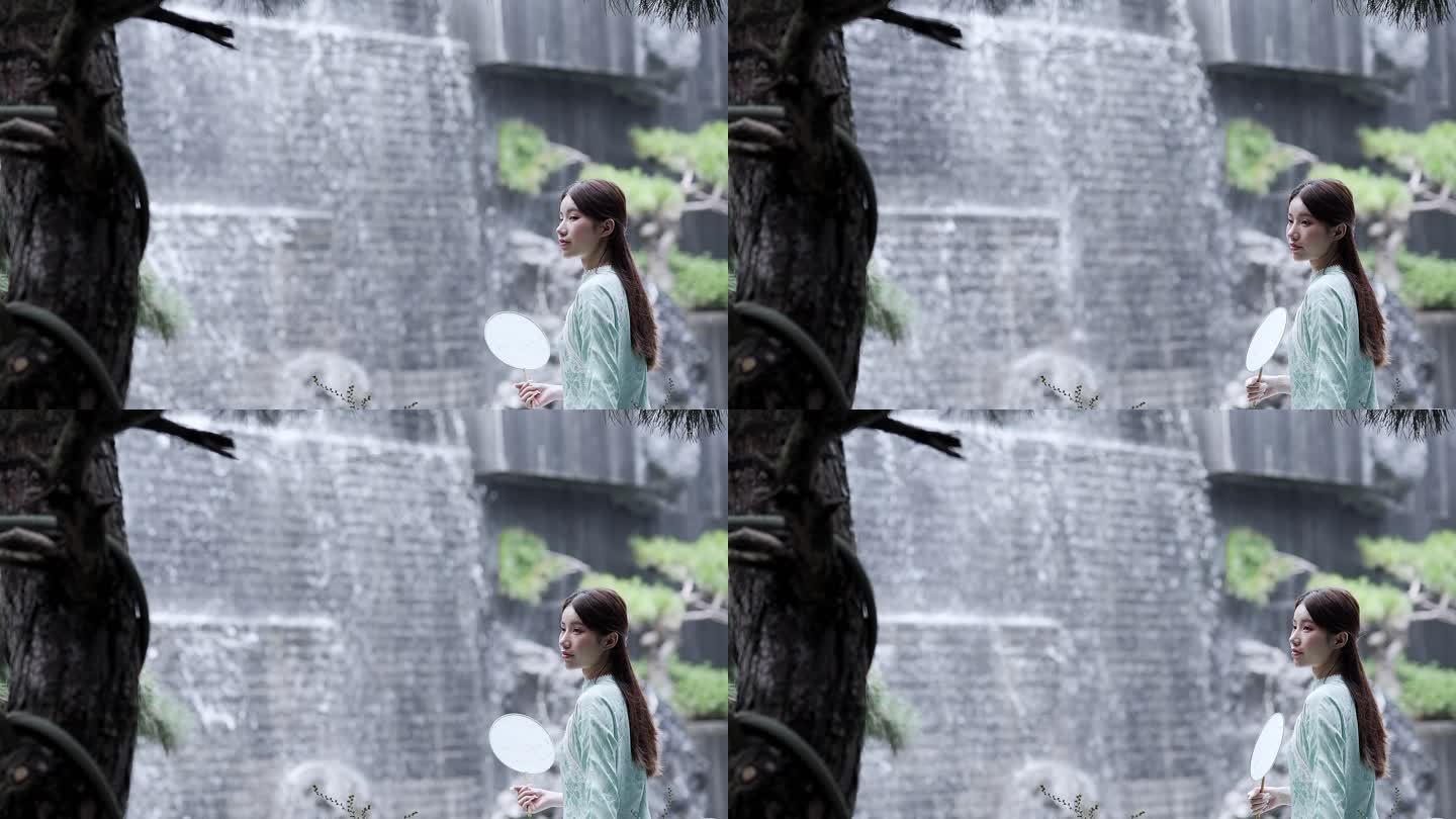 身穿汉服年轻女子摇着团扇坐在水景墙瀑布前