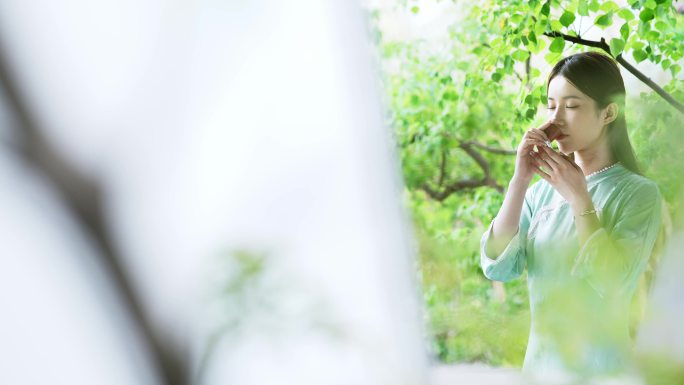 身穿汉服年轻女子在院子里端起茶杯喝茶