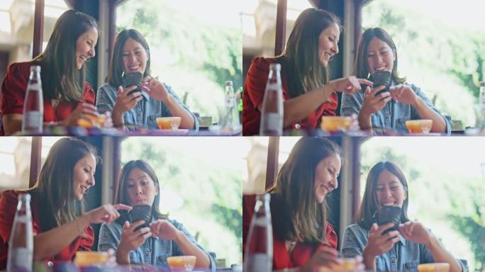 两位多民族女性朋友在咖啡馆享受时光，一起使用智能手机