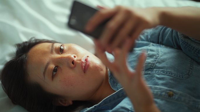 年轻女性躺在床上使用智能手机的高角度视图