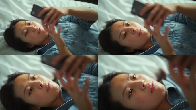 年轻女性躺在床上使用智能手机的高角度视图