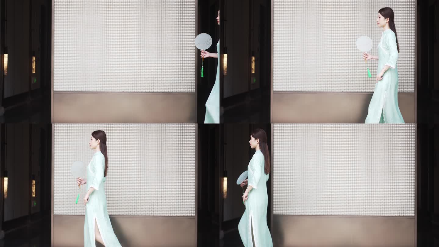 年轻旗袍女子摇着扇步行穿过中式合院门廊
