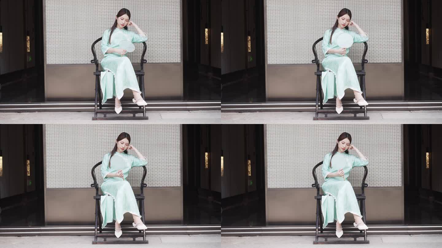 年轻旗袍女子摇着扇在中式合院门廊椅子休息