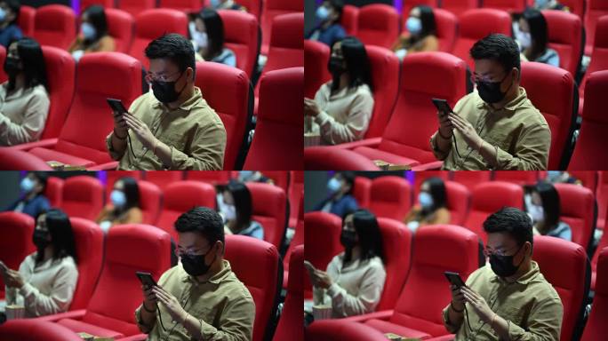 亚洲-中国混合年龄组的人坐在电影院里，使用智能手机等待电影放映时间