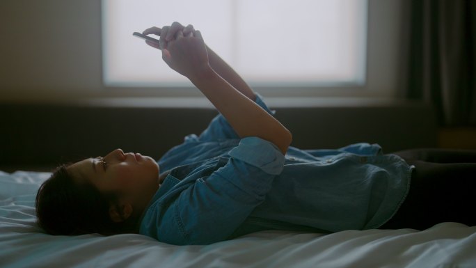 年轻女子躺在床上使用智能手机
