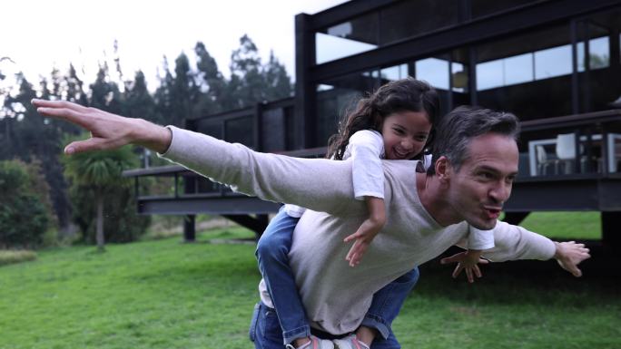 快乐的拉丁美洲父亲和女儿在户外玩飞机，两人都笑着