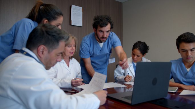一组外科医生在医疗委员会上讨论一个病例，同时查看笔记本电脑上的文件和医疗图表