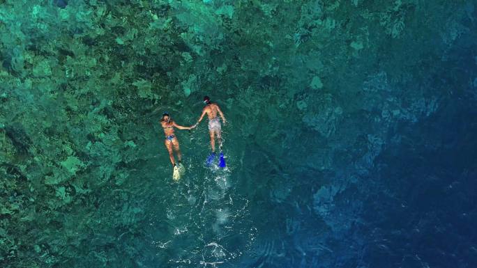 一对年轻夫妇在海洋珊瑚礁上浮潜的无人机视图