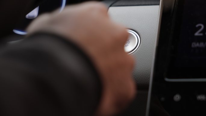一个无法辨认的人通过启动按钮启动汽车发动机的特写镜头