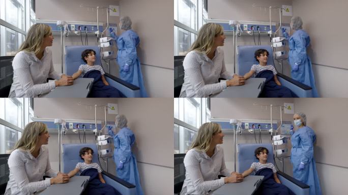 一名拉丁美洲男孩在医院接受化疗治疗时与母亲手拉手，并与护士交谈，在图表上写下自己的名字