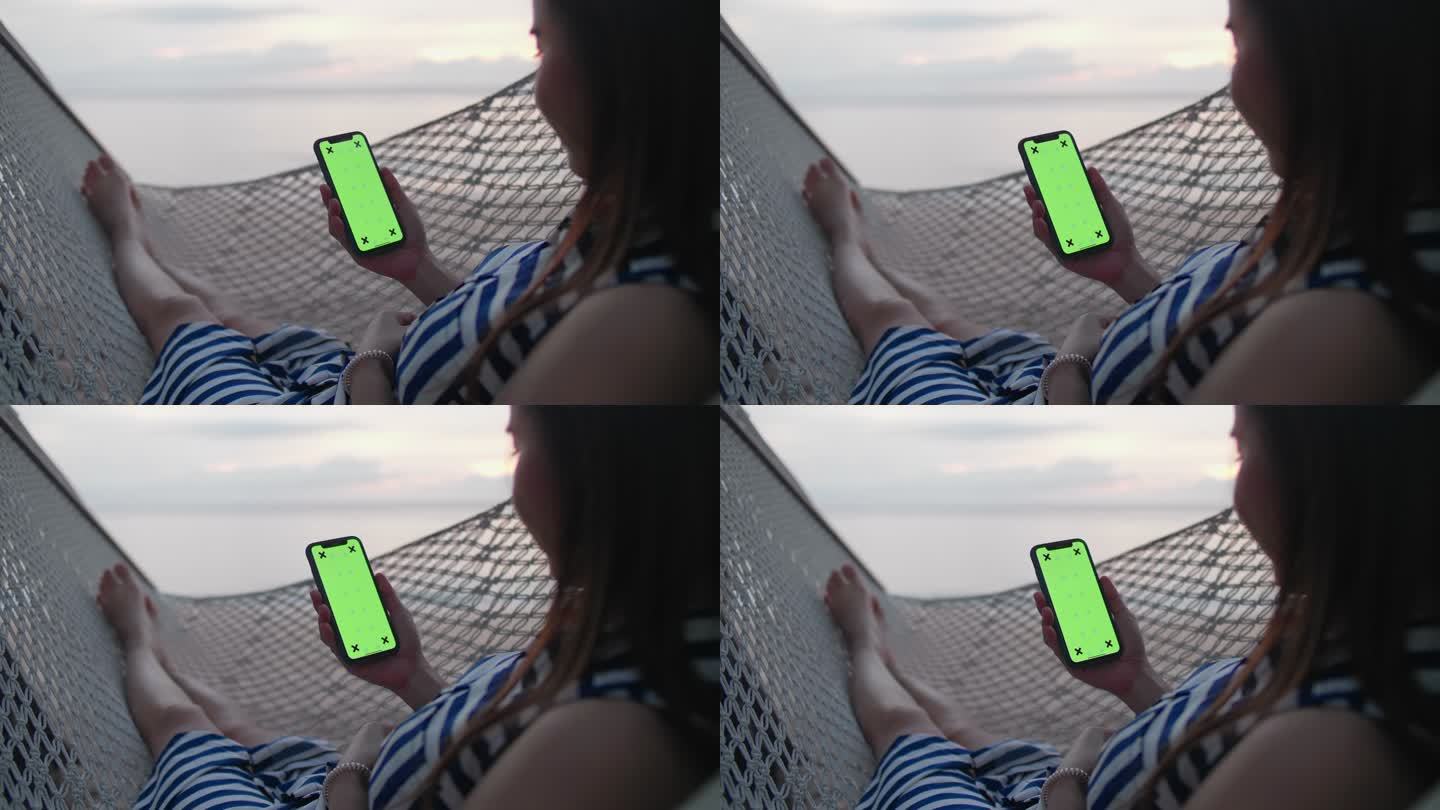 一个年轻女孩躺在海滩上的吊床上时使用智能手机