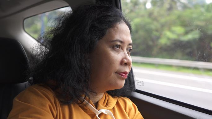 一位疲惫而忧心忡忡的妇女坐在车里看着窗外，想着自己的问题