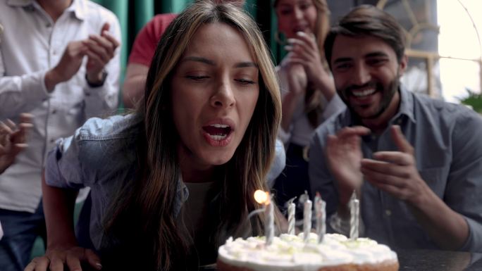 拉丁美洲人庆祝女朋友生日的特写镜头，她在酒吧吹灭蛋糕上的蜡烛