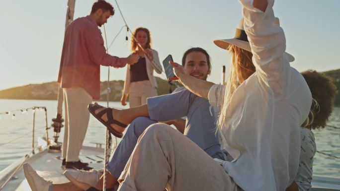 一群年轻人在日落时在船上聚会时使用智能手机