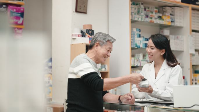 亚洲华人老年人在药房柜台使用信用卡非接触式支付