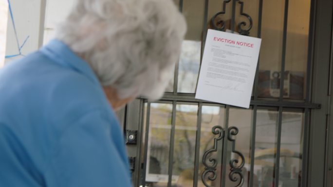 一位100岁的老年妇女站在家门口看着一张驱逐通知