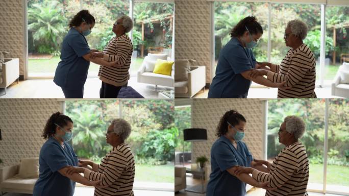 家庭护理人员帮助一名老年妇女站在家中-医生戴着防护面罩