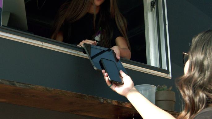 一名年轻女子在食品卡车上使用智能手机进行NFC移动无现金支付