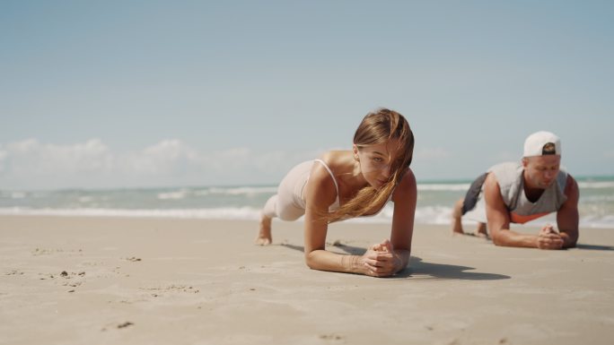 运动：男人和女人在海滩上做瑜伽板姿势