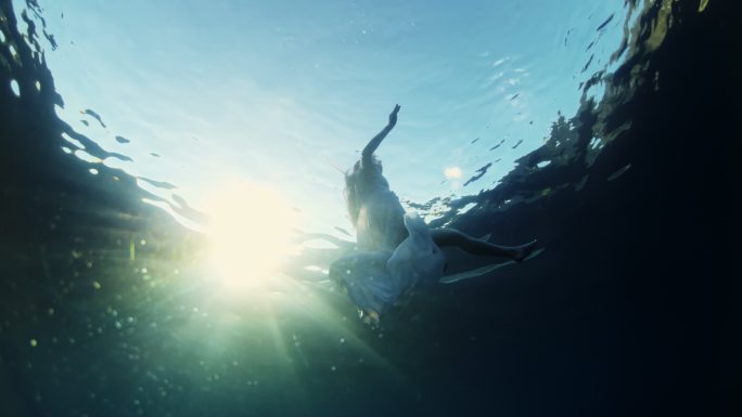 SLO-MO，一个穿着白色衣服的年轻女子在日落时在海里游泳