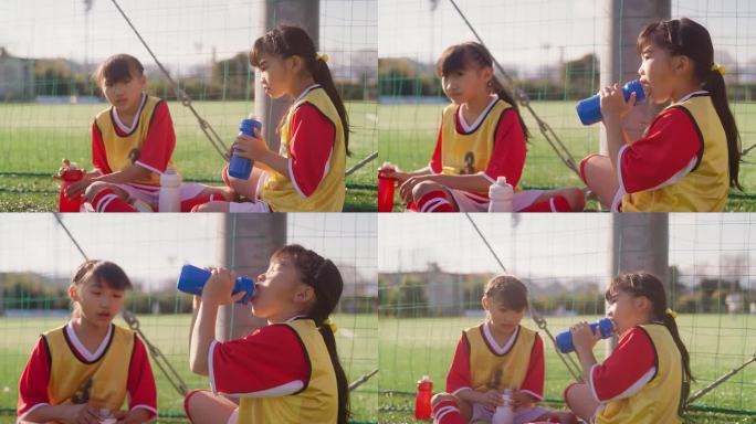 两名女童足球队或足球队队员在训练期间休息并喝水，同时享受彼此交谈的乐趣