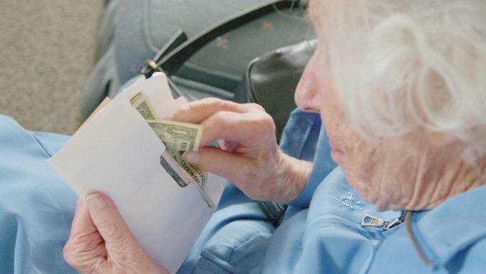 一位年长的高加索妇女看着一张一美元的钞票，同时数着信封里的现金