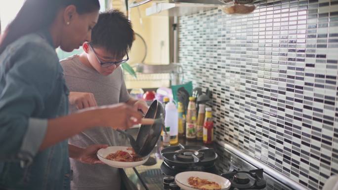 亚裔中国少年在厨房做饭，他的印度养母在厨房