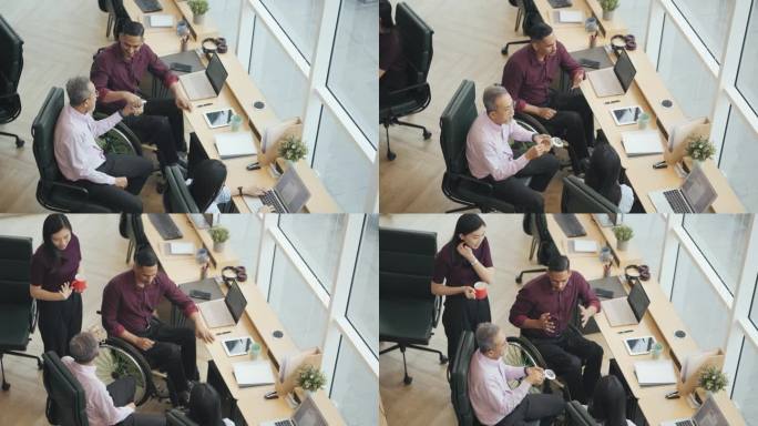 一位亚洲残疾白领正在休息，与同事一起在工作站办公室吃零食