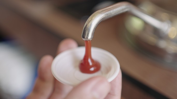 一名男子的手正在往塑料杯中注入番茄酱。
