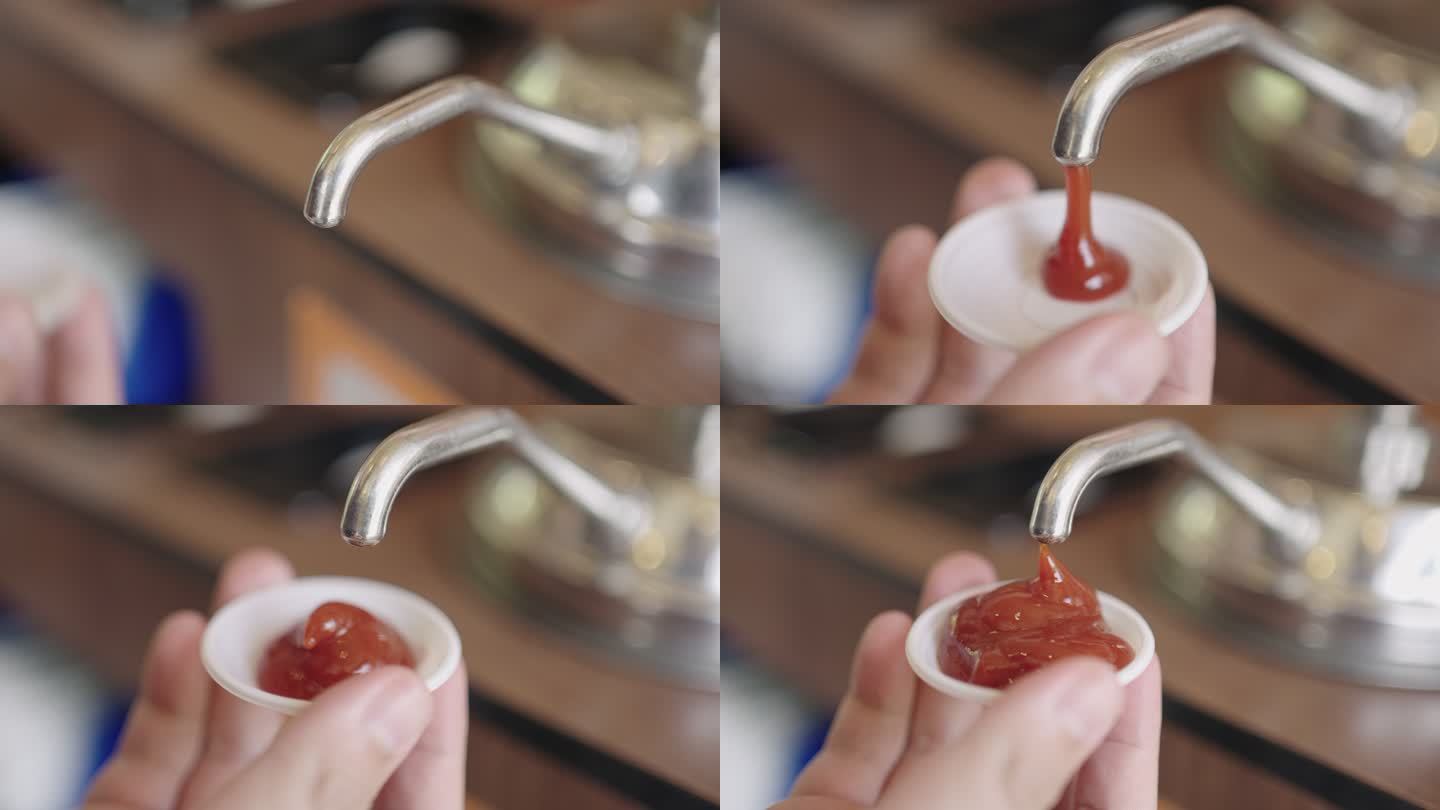 一名男子的手正在往塑料杯中注入番茄酱。