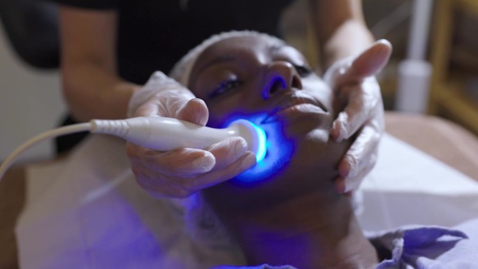 一位非洲裔美国妇女在水疗中心接受超声波和光疗法的面部恢复治疗