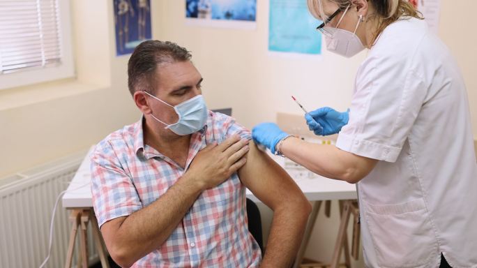 一名成年男子坐在医生办公室，由女医务工作者接种新冠疫苗