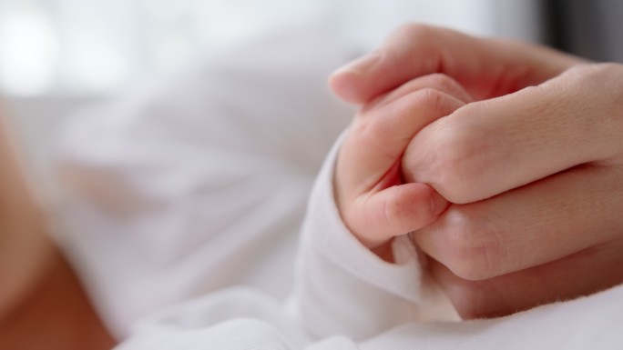 特写新生儿在家睡觉时握住母亲的手指。人寿保险、护理、保护