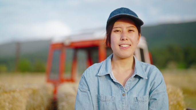 年轻的女农民坐在干草堆上的拖拉机拖车上，在农田里休息