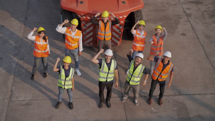 鸟瞰：一群年轻的团队在集装箱仓库行业工厂工作，举起手来代表成功的工作