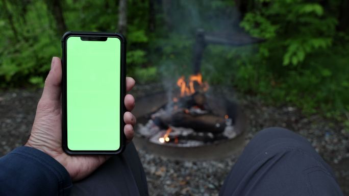 营火旁的彩色键绿色屏幕手机上的人手阅读特写