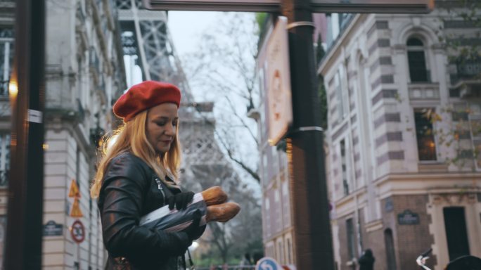 SLO-MO：一位穿着皮夹克的法国妇女沿着埃菲尔铁塔沿街携带法式面包