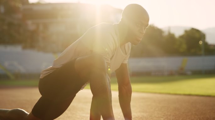 SLO MO，一名非洲裔美国人，在夕阳下的跑道上，在体育场里伸展身体